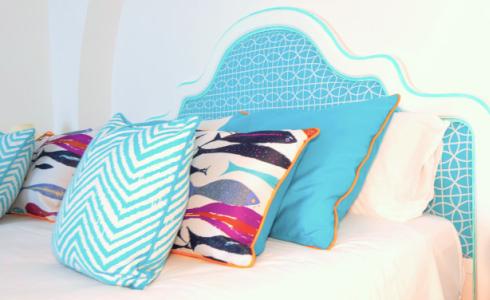 Letto con testiera azzurra e cuscini colorati, tema marino e geometrico.