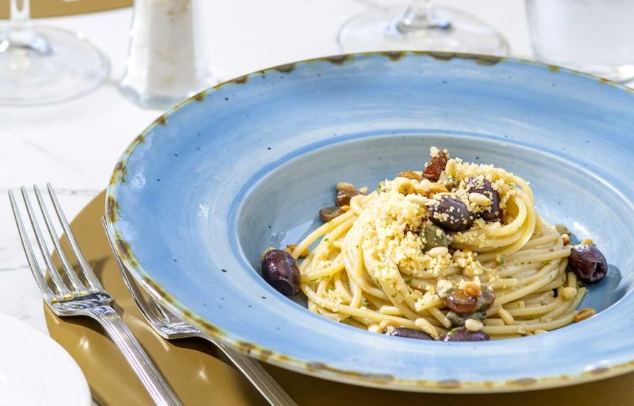 Spaghetti con olive, pinoli e pangrattato in un piatto blu elegante.